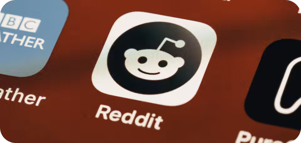 "Close-up of the Reddit app icon on a mobile screen, featuring a smiling alien mascot, 'Snoo,' in white on a black background, with the word 'Reddit' displayed underneath."