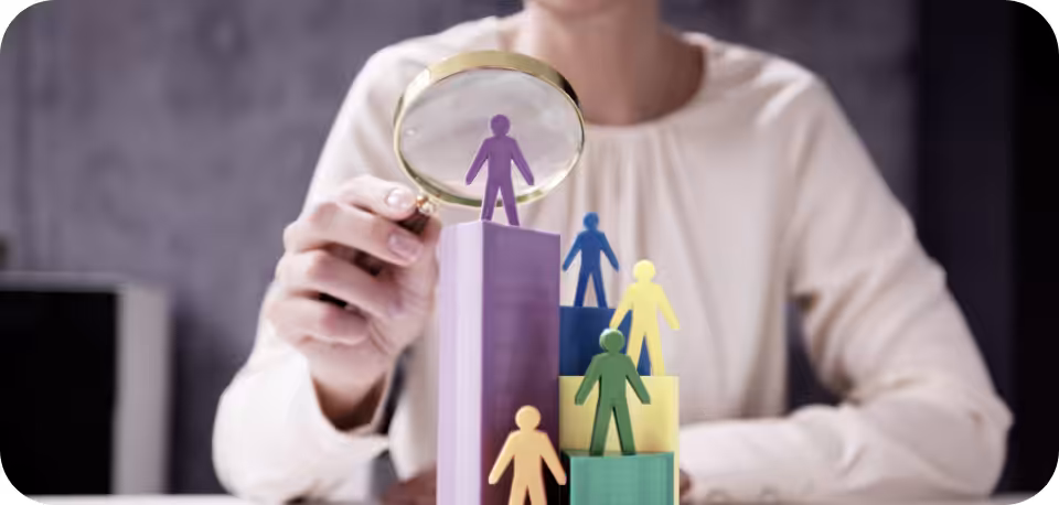 A professional examining colorful human figurines on stacked blocks with a magnifying glass, symbolizing talent evaluation, recruitment, and workforce analysis.