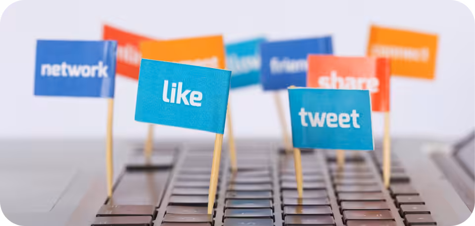 Colourful miniature flags with social media terms like 'like,' 'tweet,' 'share,' and 'network' placed on a computer keyboard, symbolising digital engagement and online interaction