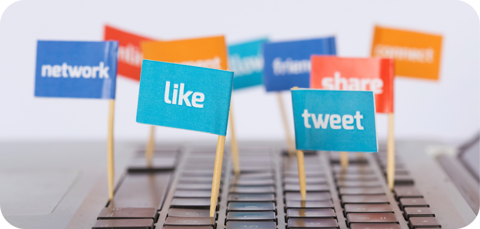 Colourful miniature flags with social media terms like 'like,' 'tweet,' 'share,' and 'network' placed on a computer keyboard, symbolising digital engagement and online interaction