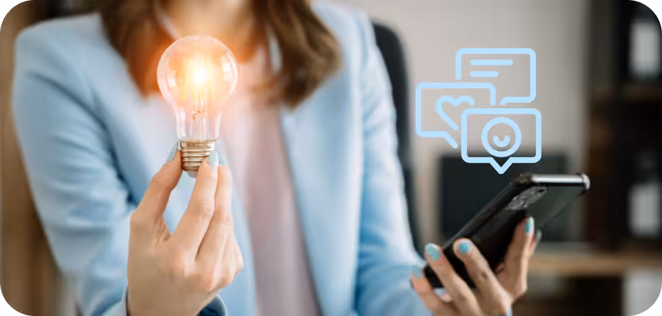 Businesswoman in a light blue blazer holding a glowing lightbulb while using a smartphone, symbolizing innovative strategies for combining organic and paid social media marketing, with social engagement icons floating beside her.